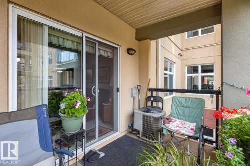 Covered patio with a stucco exterior, featuring a sliding glass door with a screen, and an exterior wall sconce - #210 7909 71 St Nw, Edmonton, AB - Outdoor With Exterior