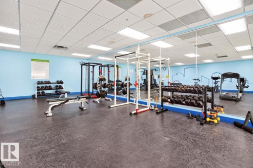 Spacious fitness area featuring rubberized flooring, mirrored wall, and overhead lighting - #210 7909 71 St Nw, Edmonton, AB - Indoor Photo Showing Gym Room