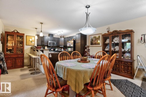 Open-concept layout with a kitchen featuring dark wood-finish cabinetry, stainless steel appliances, and a breakfast bar with pendant lighting - #210 7909 71 St Nw, Edmonton, AB - Indoor Photo Showing Dining Room