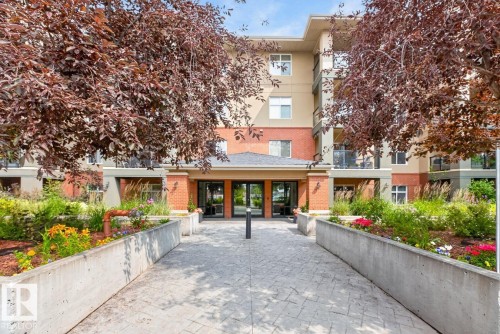 Multi-story building featuring a brick and stucco facade, a covered entry with double glass doors, and a paved walkway - #210 7909 71 St Nw, Edmonton, AB - Outdoor With Balcony