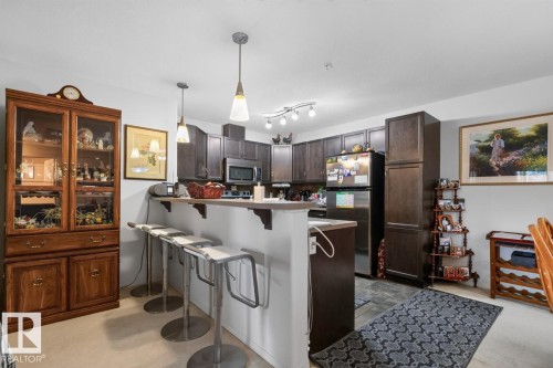 Kitchen area with dark wood-finish cabinetry, stainless steel appliances, and a breakfast bar - #210 7909 71 St Nw, Edmonton, AB - Indoor Photo Showing Kitchen