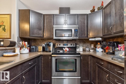 U-shaped kitchen featuring wood-finish cabinetry, stainless steel appliances, and a tiled backsplash - #210 7909 71 St Nw, Edmonton, AB - Indoor Photo Showing Kitchen