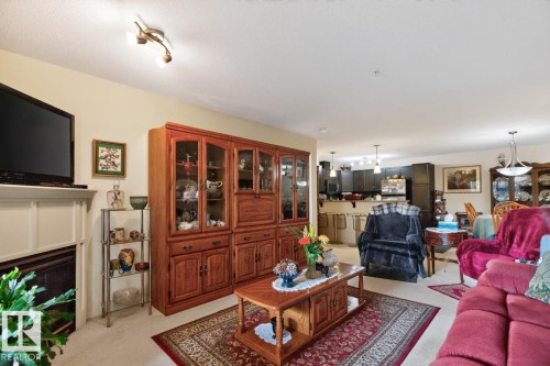 Neutral wall paint, carpeted flooring, track lighting, and a built-in fireplace - #210 7909 71 St Nw, Edmonton, AB - Indoor Photo Showing Living Room With Fireplace