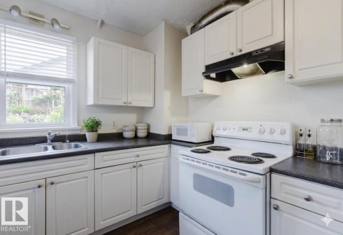 Efficient galley kitchen featuring white cabinetry, black countertops, electric range with oven, undermount sink, and a window overlooking outdoor space - 12223 127 Street Nw, Edmonton, AB - Indoor Photo Showing Kitchen With Double Sink