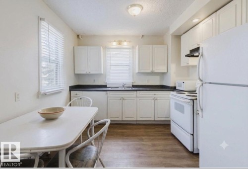 Kitchen featuring wood-finish flooring, white cabinetry, dark countertops, and white appliances - 12223 127 Street Nw, Edmonton, AB - Indoor Photo Showing Kitchen
