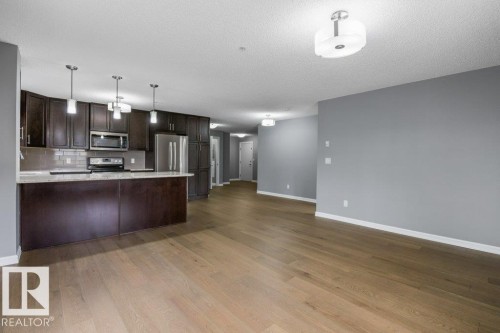 Open-concept kitchen with dark wood-finish cabinetry, stainless steel appliances, and pendant lighting - #117 2203 44 Av Nw, Edmonton, AB - Indoor Photo Showing Kitchen
