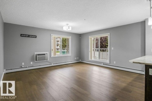 Wood-finish flooring throughout, light gray wall finishes, flush mount ceiling light fixture, and a built-in air conditioning unit - #117 2203 44 Av Nw, Edmonton, AB - Indoor Photo Showing Living Room