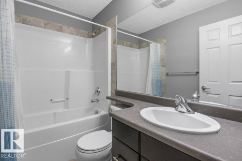 Bathroom featuring a white integrated tub and shower unit, a dark wood-finish vanity with an integrated sink, a large wall mirror, and a white paneled door - #117 2203 44 Av Nw, Edmonton, AB - Indoor Photo Showing Bathroom