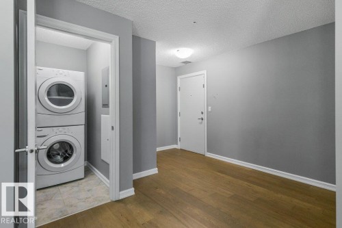 Wood-finish flooring, stackable laundry appliances, and a flush-mount ceiling light - #117 2203 44 Av Nw, Edmonton, AB - Indoor Photo Showing Laundry Room