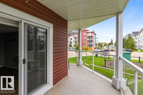 Concrete patio with glass panel railing and white posts, featuring a white frame sliding door and red horizontal siding - #117 2203 44 Av Nw, Edmonton, AB - Outdoor With Deck Patio Veranda With Exterior