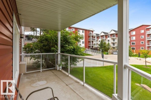 Covered concrete patio with glass panel railing and white posts - #117 2203 44 Av Nw, Edmonton, AB - Outdoor With Exterior