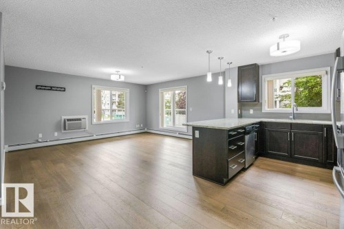 Open-concept living space featuring wood-finish flooring, dark wood cabinetry, stainless steel appliances, and a kitchen island with pendant lighting - #117 2203 44 Av Nw, Edmonton, AB - Indoor