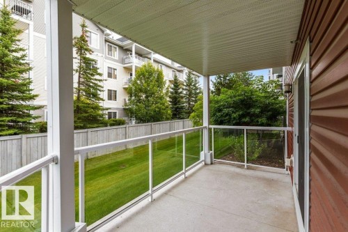 Covered outdoor patio with a concrete surface, glass panel railing, and wood-paneled exterior wall - #117 2203 44 Av Nw, Edmonton, AB - Outdoor With Exterior