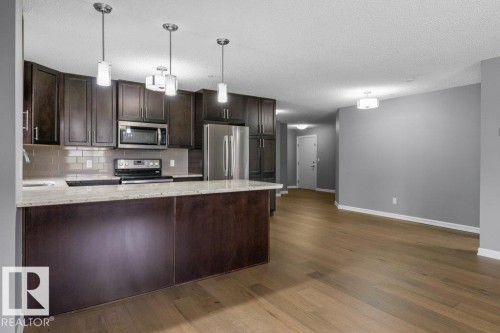 Kitchen featuring dark wood cabinetry, light-toned countertops, stainless steel appliances, and subway tile backsplash - #117 2203 44 Av Nw, Edmonton, AB - Indoor Photo Showing Kitchen With Upgraded Kitchen