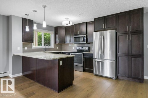 Kitchen featuring wood-finish flooring, dark wood cabinetry, stainless steel appliances, and light-toned countertops - #117 2203 44 Av Nw, Edmonton, AB - Indoor Photo Showing Kitchen With Upgraded Kitchen
