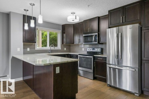 Kitchen featuring dark wood-finish cabinetry, stainless steel appliances, light-toned countertops, and wood-finish flooring - #117 2203 44 Av Nw, Edmonton, AB - Indoor Photo Showing Kitchen With Upgraded Kitchen