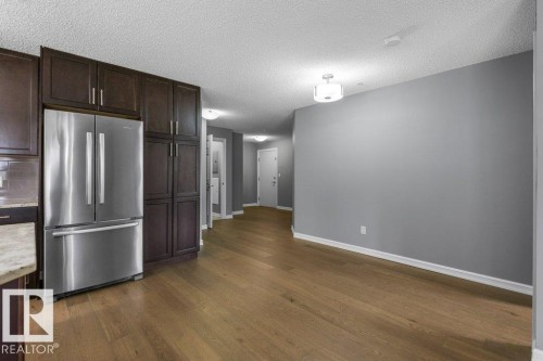 Stainless steel refrigerator, dark wood cabinetry, wood-finish flooring, light gray wall paint, and a semi-flush mount ceiling light - #117 2203 44 Av Nw, Edmonton, AB - Indoor Photo Showing Other Room