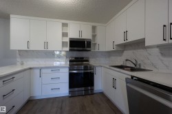 Modern kitchen featuring white cabinetry, quartz countertops, a tile backsplash, stainless steel appliances, and wood-finish flooring - 