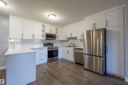 White cabinetry, stainless steel appliances, wood-finish flooring, quartz countertops, and a white tile backsplash - 