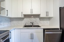 Sleek kitchen featuring white cabinetry, light-toned countertops, and a patterned tile backsplash - 