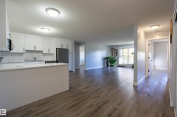 Open-concept living area featuring wood-finish flooring, white cabinetry, a built-in kitchen island, and a stainless steel refrigerator - 