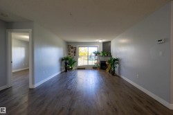 Spacious room featuring wood-finish flooring, light gray wall paint, a corner fireplace with a dark tile surround, and a large window - 