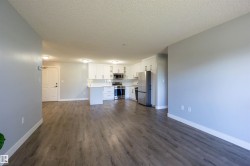 Open-concept layout featuring wood-finish flooring, a kitchen with white cabinetry, stainless steel appliances, and a peninsula with seating - 
