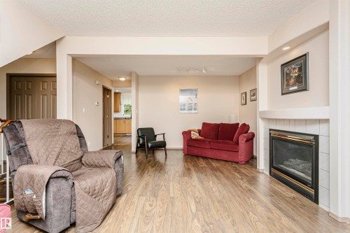 Living space featuring wood-finish flooring, a white tiled fireplace, and a built-in recessed ceiling light - #42 9630 176 St Nw, Edmonton, AB - Indoor Photo Showing Living Room With Fireplace