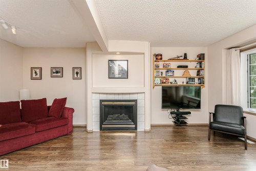 Wood-finish flooring throughout, featuring a tiled fireplace with mantel, built-in shelving, and a prominent window - #42 9630 176 St Nw, Edmonton, AB - Indoor Photo Showing Living Room With Fireplace