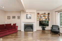 Wood-finish flooring throughout, featuring a tiled fireplace with mantel, built-in shelving, and a prominent window - 