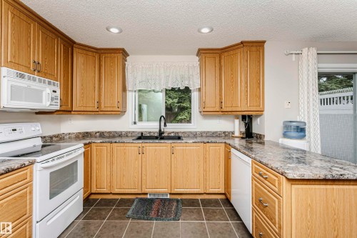 U-shaped kitchen with wood-finish cabinetry, dark countertop, ceramic tile flooring, and integrated appliances - #42 9630 176 St Nw, Edmonton, AB - Indoor Photo Showing Kitchen With Double Sink