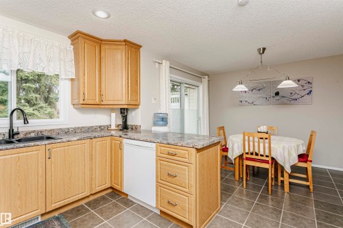 Kitchen featuring wood-finish cabinetry, speckled countertops, a black gooseneck faucet, and a built-in dishwasher - #42 9630 176 St Nw, Edmonton, AB - Indoor