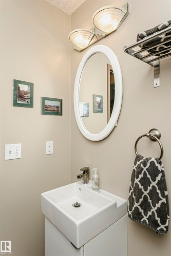 Rectangular vessel sink with a single-handle chrome faucet, oval wall-mounted mirror, and a wall-mounted light fixture - #42 9630 176 St Nw, Edmonton, AB - Indoor Photo Showing Bathroom