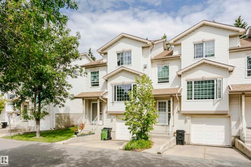 Townhome exterior with light-colored siding, multiple windows, attached garage, and prominent front entry - #42 9630 176 St Nw, Edmonton, AB - Outdoor With Facade