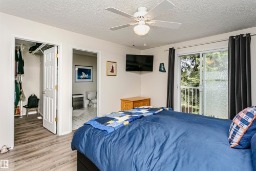 Wood-finish flooring, ceiling fan, white paneled doors, sliding glass door to exterior, and wall-mounted television - #42 9630 176 St Nw, Edmonton, AB - Indoor Photo Showing Bedroom