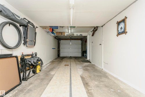 Concrete flooring with central textured strips, white painted walls, and a roll-up garage door - #42 9630 176 St Nw, Edmonton, AB - Indoor Photo Showing Garage