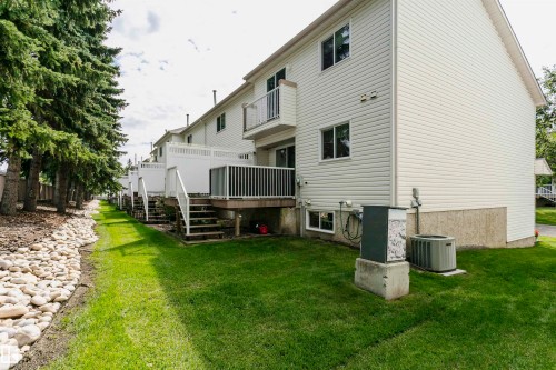 Exterior featuring white siding, multiple balconies with white railings, a ground-level patio, and a manicured lawn - #42 9630 176 St Nw, Edmonton, AB - Outdoor With Deck Patio Veranda