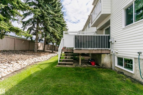 Rear exterior with white vinyl siding, a wood-finish deck with white railings, and a concrete foundation with a basement window - #42 9630 176 St Nw, Edmonton, AB - Outdoor With Deck Patio Veranda