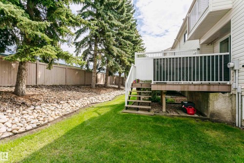 Expansive green lawn with a white composite deck and stairs, featuring natural rock landscaping and mature evergreen trees - #42 9630 176 St Nw, Edmonton, AB - Outdoor With Deck Patio Veranda