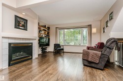 Living area featuring wood-finish flooring, a tiled fireplace with mantel, built-in shelving, a large bay window, and a white railing - 