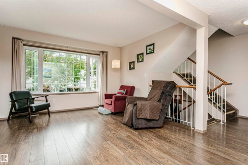 Wood-finish flooring throughout, large multi-pane window, staircase with wood handrails, and a contemporary pendant light fixture - #42 9630 176 St Nw, Edmonton, AB - Indoor Photo Showing Living Room