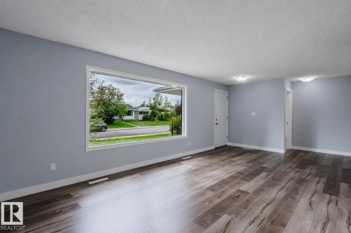 Spacious room featuring wood-finish flooring, a large picture window, and light blue painted walls - 11420 46 Avenue Nw, Edmonton, AB - Indoor Photo Showing Other Room