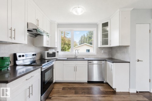 White shaker cabinetry, stainless steel appliances, dark countertops, wood-finish flooring, and a tiled backsplash - 11420 46 Avenue Nw, Edmonton, AB - Indoor Photo Showing Kitchen