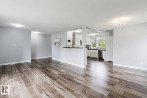 Wood-finish flooring throughout, recessed lighting, and a kitchen featuring white cabinetry, a double-basin sink, and stainless steel appliances - 11420 46 Avenue Nw, Edmonton, AB - Indoor