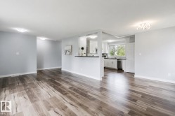 Wood-finish flooring throughout, recessed lighting, and a kitchen featuring white cabinetry, a double-basin sink, and stainless steel appliances - 