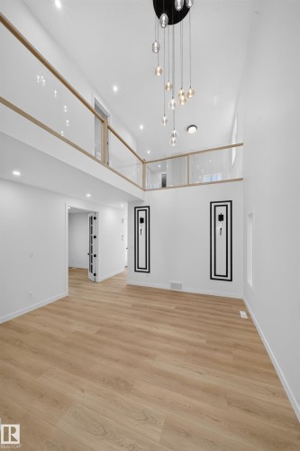 Vaulted ceiling with an elaborate chandelier, wood-finish flooring, recessed lighting, and a glass-paneled railing - 8915 Mayday Way Sw, Edmonton, AB - Indoor Photo Showing Other Room