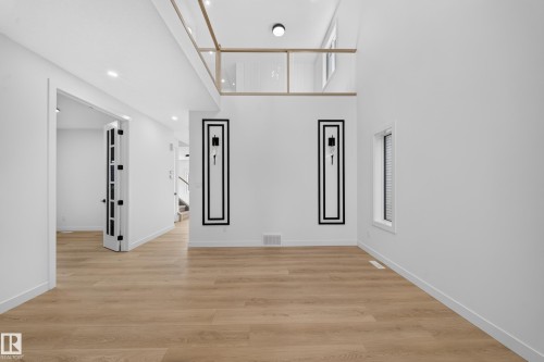 High ceilings with recessed lighting, wood-finish flooring, and a second-story interior balcony with glass railing - 8915 Mayday Way Sw, Edmonton, AB - Indoor Photo Showing Other Room
