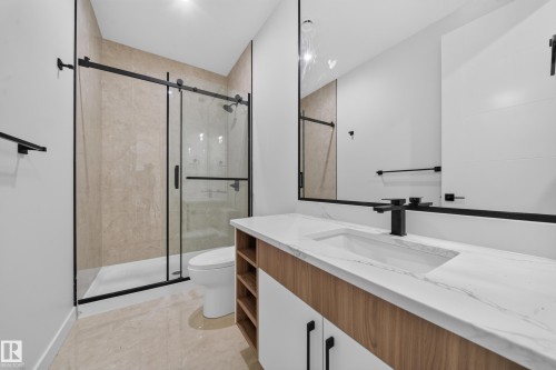 Tiled shower with a sliding glass door and matte black fixtures, wood-finish vanity with an integrated sink, and a large wall mirror - 8915 Mayday Way Sw, Edmonton, AB - Indoor Photo Showing Bathroom