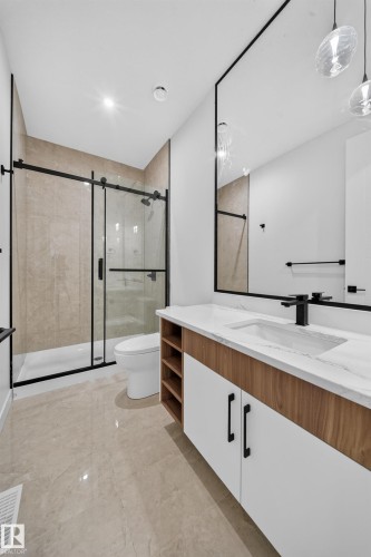 Spacious bathroom featuring a floating vanity with wood-finish and white cabinetry, a large mirrored wall, and a glass-enclosed shower with a black frame - 8915 Mayday Way Sw, Edmonton, AB - Indoor Photo Showing Other Room