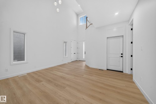 High ceilings featuring a modern chandelier, wood-finish flooring, white walls, and contemporary doors - 8915 Mayday Way Sw, Edmonton, AB - Indoor Photo Showing Other Room